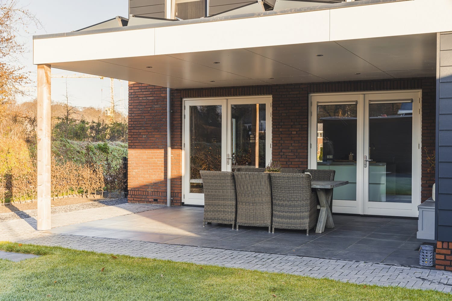 Woning met dubbele houten tuindeuren onder overkapping, geplaatst in een bakstenen gevel en voorzien van royale glasvlakken – Toelevering Online