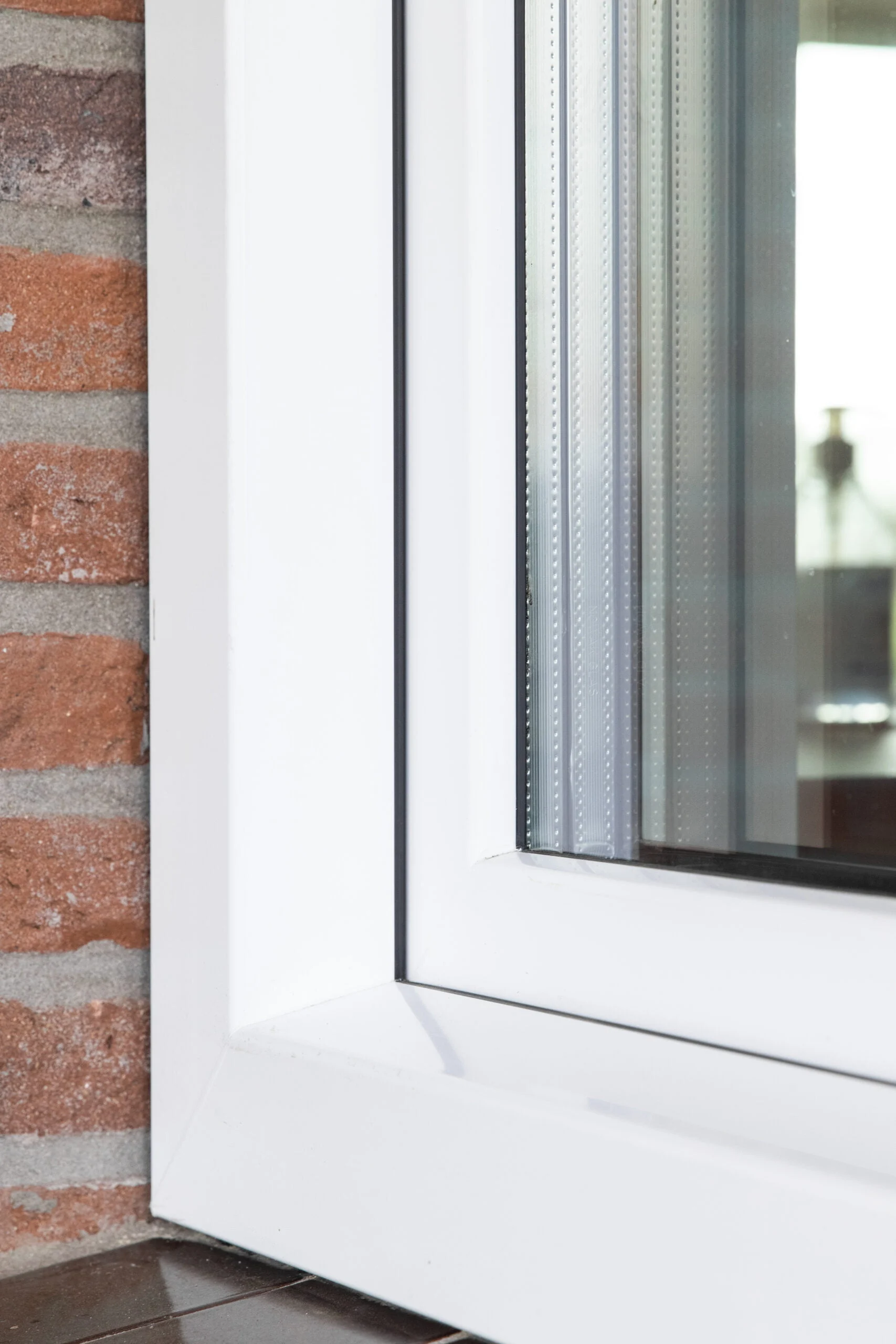 Binnenhoek van een wit kunststof kozijn, geplaatst tegen een gemetselde muur.